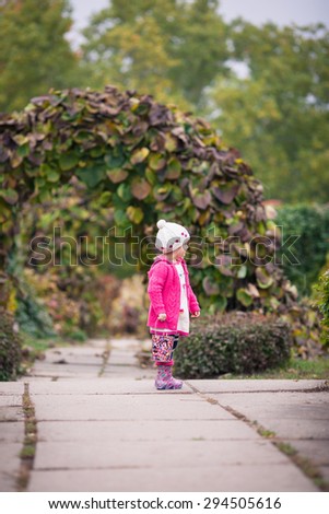 Little girl in bright clothes stand  in autumn garden. Baby holds bright colored pail and smile