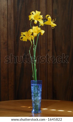 Blue glass vase with glass stones and tall daylilies on oak table.