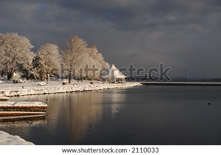 Park covered with winter snow in dark skies and dark lake.