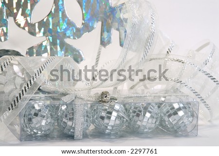 Platinum and diamond engagement and wedding rings on box of mirrored silver ornaments with ribbons and iridescent snowflakes in the background.