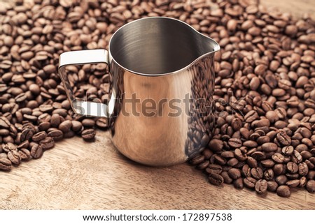 coffee parts stainless steel latte pitcher and beans on old wooden table