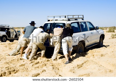 Few people pushing a car that stuck in the sand while safari desert