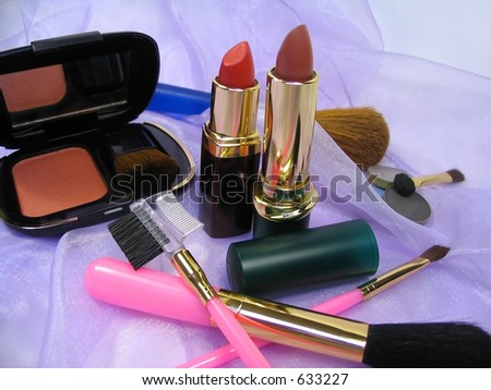 Various cosmetic products and brushes over shiny lilac fabric