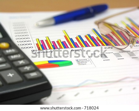 Colorful sales charts, calculator, blue pen and glasses. Shallow DOF, focus on charts