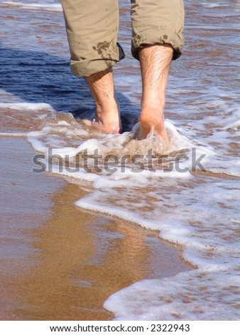 stock photo Male feet with rolled up pants wading on the shoreline