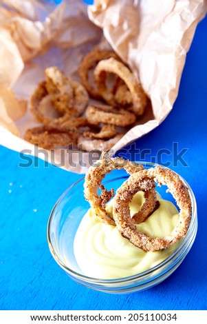 Baked onion rings with mayonnaise sauce on blue background - healthy fast food variation of famous dish.