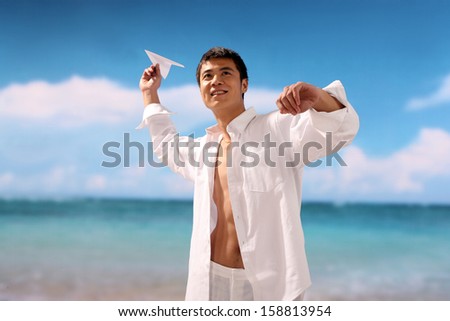 Man playing paper airplane on beach,smiling