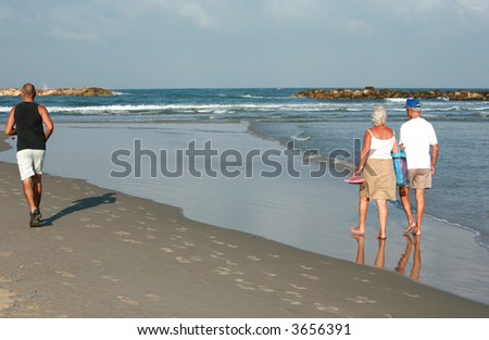 old couple walking in the sea and an early morning runner ,running on the sand
