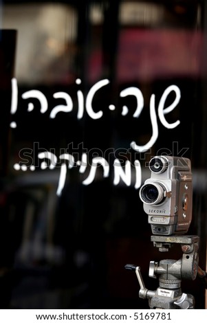old 8mm camera on a tripod in front of an antique shop .On the shop's window it's written in hebrew