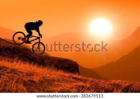 silhouette of downhill mountain bike rider at orange sunset