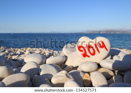 2014  new year written on heart shaped stone on the beach with spray brush