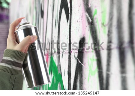 Human hand holding a graffiti Spray can in front of a colorful wall