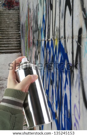 Human hand holding a graffiti Spray can in front of a colorful wall