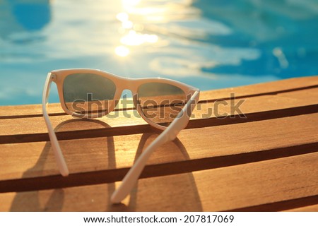 Sunglasses on wooden planks and water on sunset