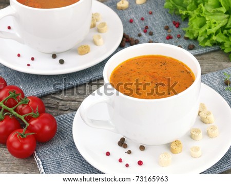 Tomato soup with fresh ingredients in a soup cup, over an old wooden background