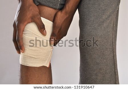 Closeup of male athlete clutching knee wrapped in sports bandage on grey background