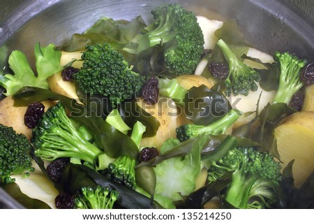 Closeup of steaming pot of vegetables including broccoli, potato, kombu, and raisins