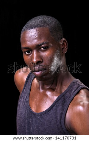 Portrait of bold, determined, sweaty, athletic, young black man on black background
