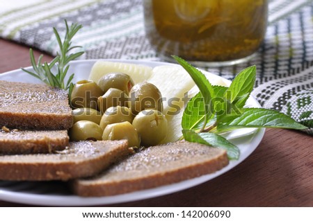 Healthy and nutritious plate of Mediterranean diet food including stuffed green olives, whole wheat bread, European cheese, mint leaves, rosemary, and olive oil