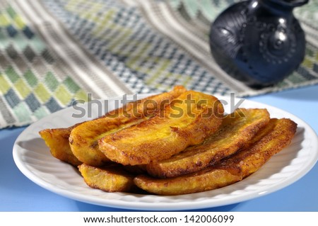 Stack of fried sliced plantain bananas on plate with attractive traditional Mexican background