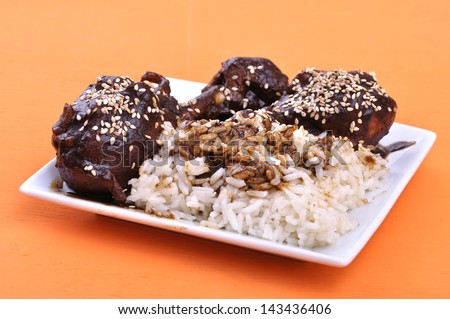 Traditional Mexican dish of chicken and white rice topped with dark mole sauce and sesame seed on orange table