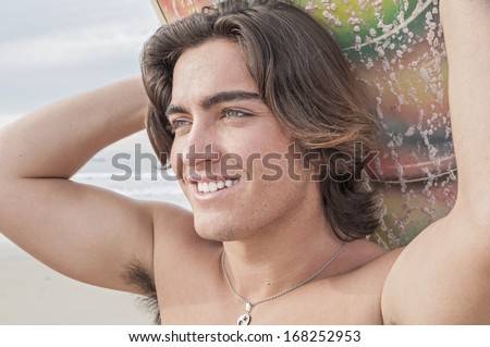 Closeup of handsome young Caucasian male surfer carrying surfboard on head as he walks on beach