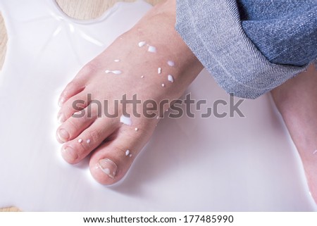 Closeup of young child\'s bare foot stepping in puddle of spilled milk on floor