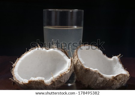 Fresh young coconut in broken shell with glass of coconut water on platter with black background