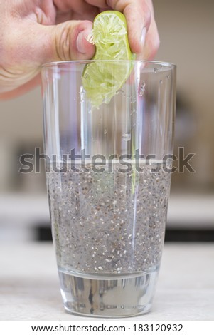 Hand squeezes lime extracting juice into glass of water and chia seed