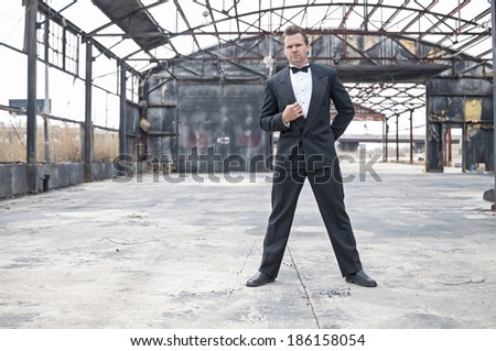 Formal dressed tough Caucasian man stands ready in action pose in burned down warehouse
