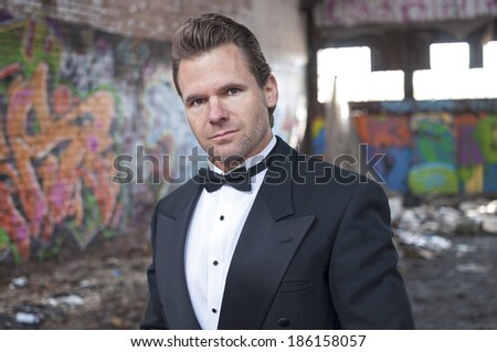 Well dressed handsome Caucasian man wearing tuxedo in trashy urban ghetto setting
