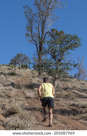 Caucasian male runner in shorts and sandals runs up steep dusty trail in dry mountains