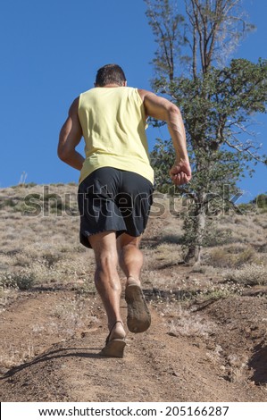 Muscular Caucasian runner in shorts and sandals runs up steep trail on hill in countryside