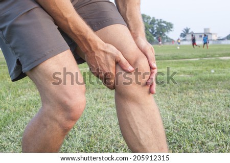 Closeup of athletic Caucasian man holding his painful knee on soccer field