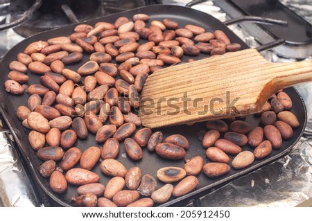 Wooden spoon stirring hot skillet on stove toasting whole cocoa beans