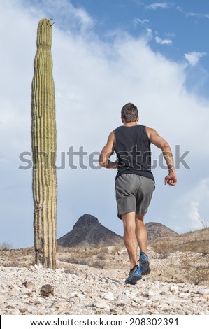 Muscular Caucasian male runner in shorts and running shoes runs across rugged rocky desert terrain