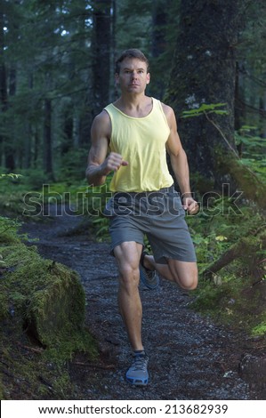 Muscular Caucasian man running in short and tank top on trail through dense forest