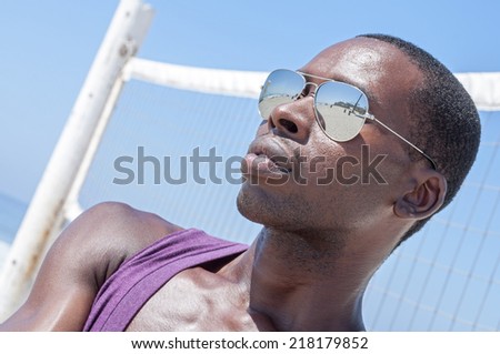 Handsome young African American man fashionably styling in cool shades in front of volley ball net on sunny beach