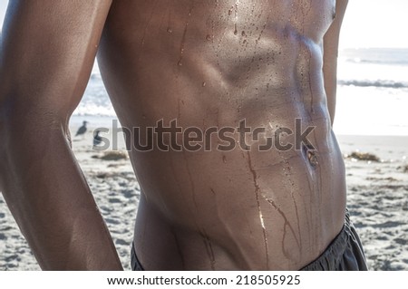 Closeup of beautiful toned abs and waist dripping with water on African American man at beach
