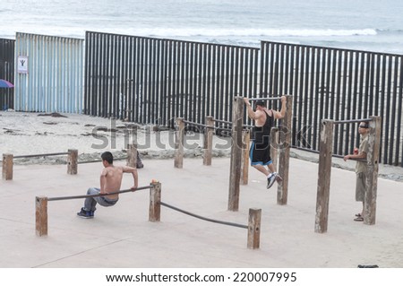 TIJUANA, MEXICO - JULY 26, 2014: Exercise enthusiasts workout with outdoor exercise equipment on the beach in Tijuana, Mexico along the border fence that separates the U.S. and Mexico