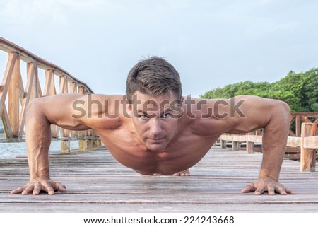 Front low angle of muscular shirtless Caucasian man performing push ups on wooden dock at beach