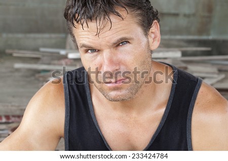Closeup portrait of unshaven sweaty Caucasian man in black tank top working in construction area