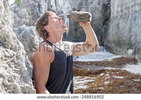 Athletic male hiker on rocky beach pours water into mouth from canteen on hot day
