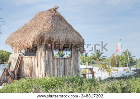 Palm-thatched hut with stick walls and hammocks inside on white sand beach in Tulum, Mexico