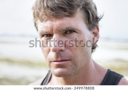 Closeup portrait of rugged Caucasian man with stern bold facial expression, distinct features, and intense predator eyes in undefined outdoor environment