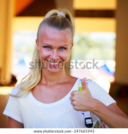 Outdoor summer portrait of beautiful young blue eyed woman in a white tee shirt and showing thumbs up