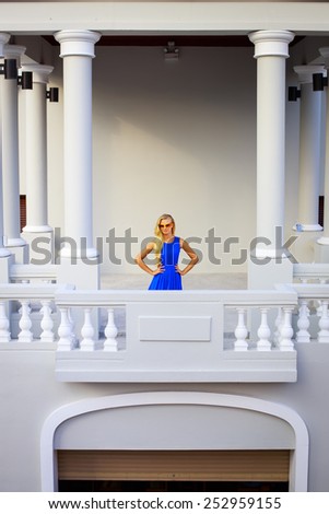 Fashion portrait of young gorgeous woman in a blue dress and sunglasses. Pretty blonde woman posing on a vintage balcony.