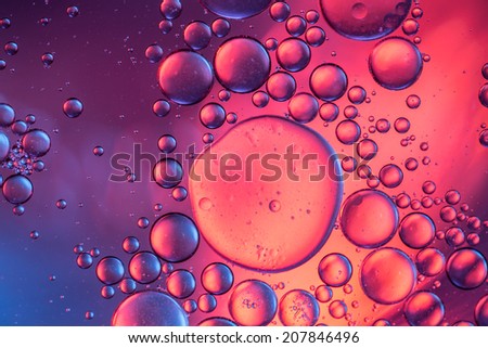 Abstract bubbles of water forming like asteroids in front of a purple and pink colored blurry background