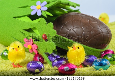 Large chocolate easter egg in green basket surrounded by smaller chocolate eggs