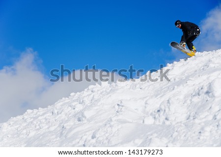Snowboarder taking off for a jump from a natural drop into a lot of snow, off piste riding in France